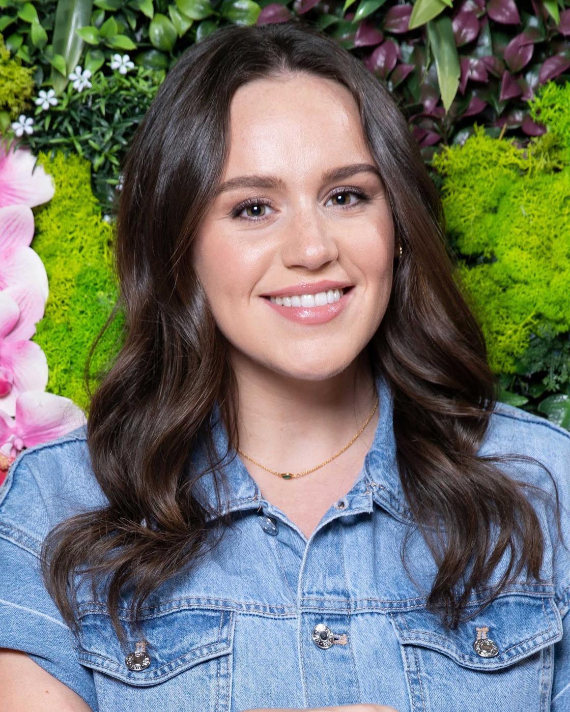 Ellie Leach sits on the ground in front of some floral displays