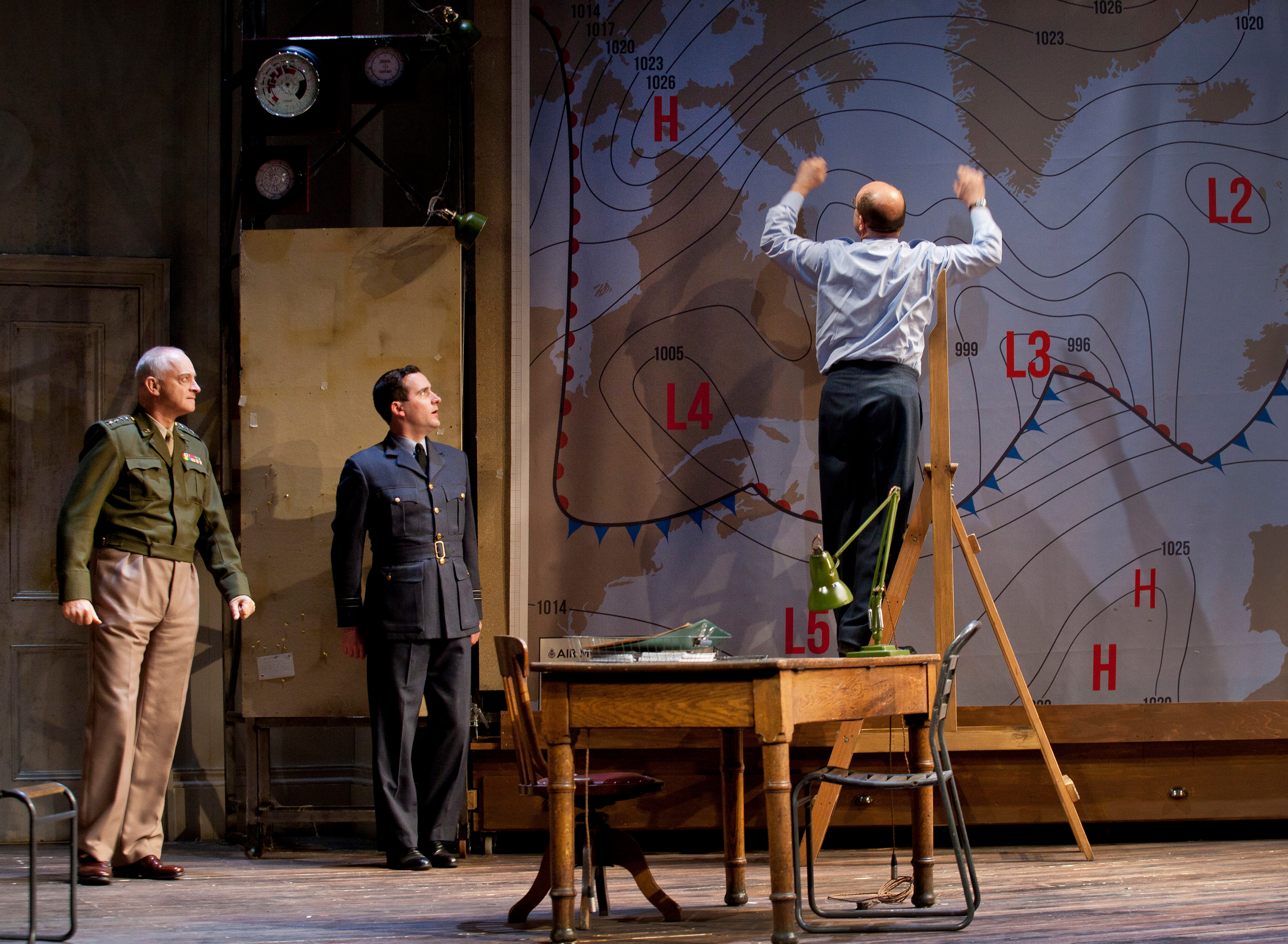 James Stagg stands on a chair in front of a weather map with others watching