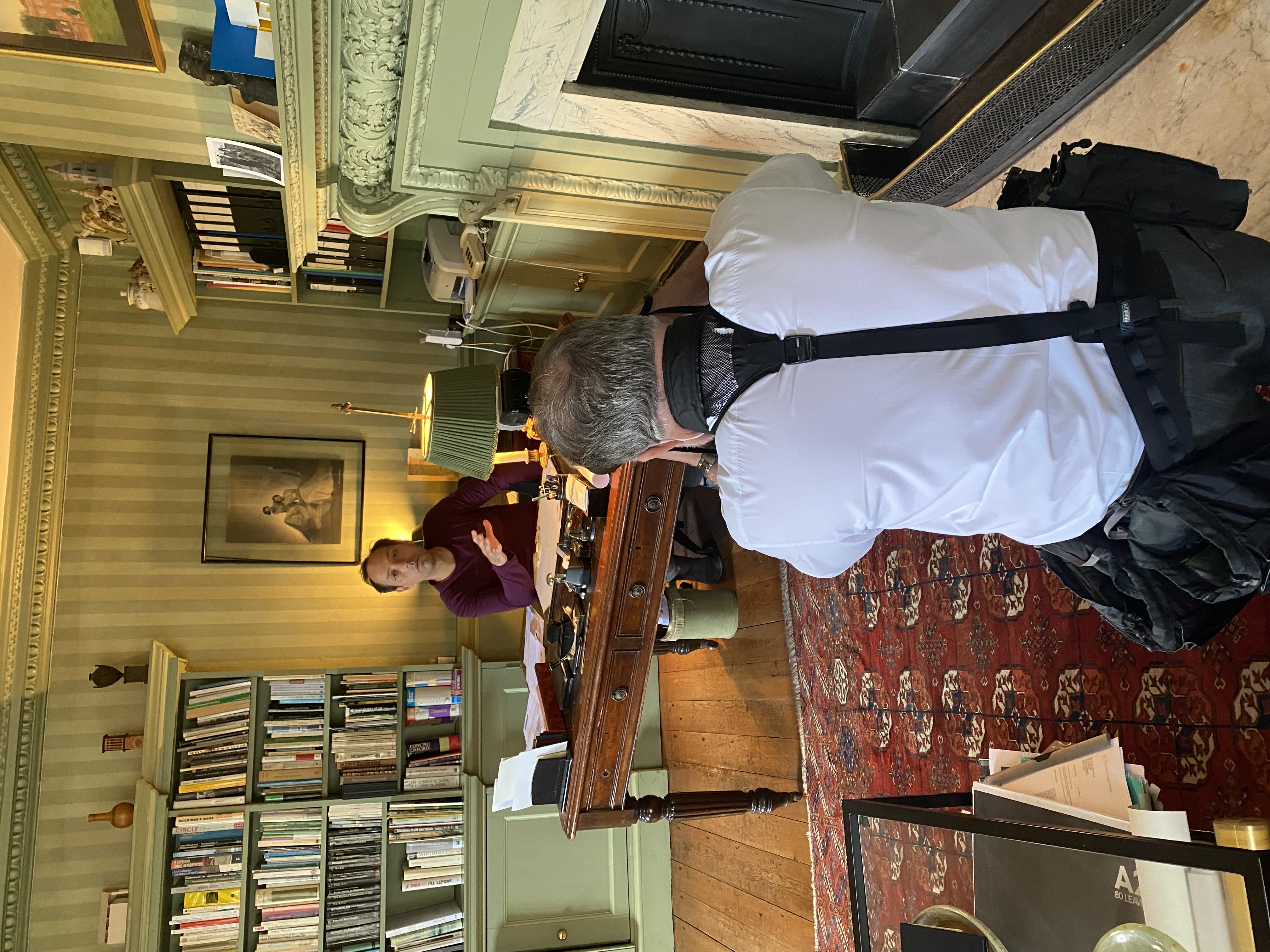 Philip Arditti sits at a library desk, a photographer takes a photo of him