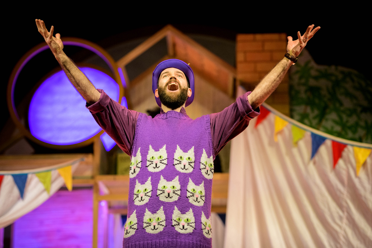 A Man in a purple cat jumper has his arms raised to the sky