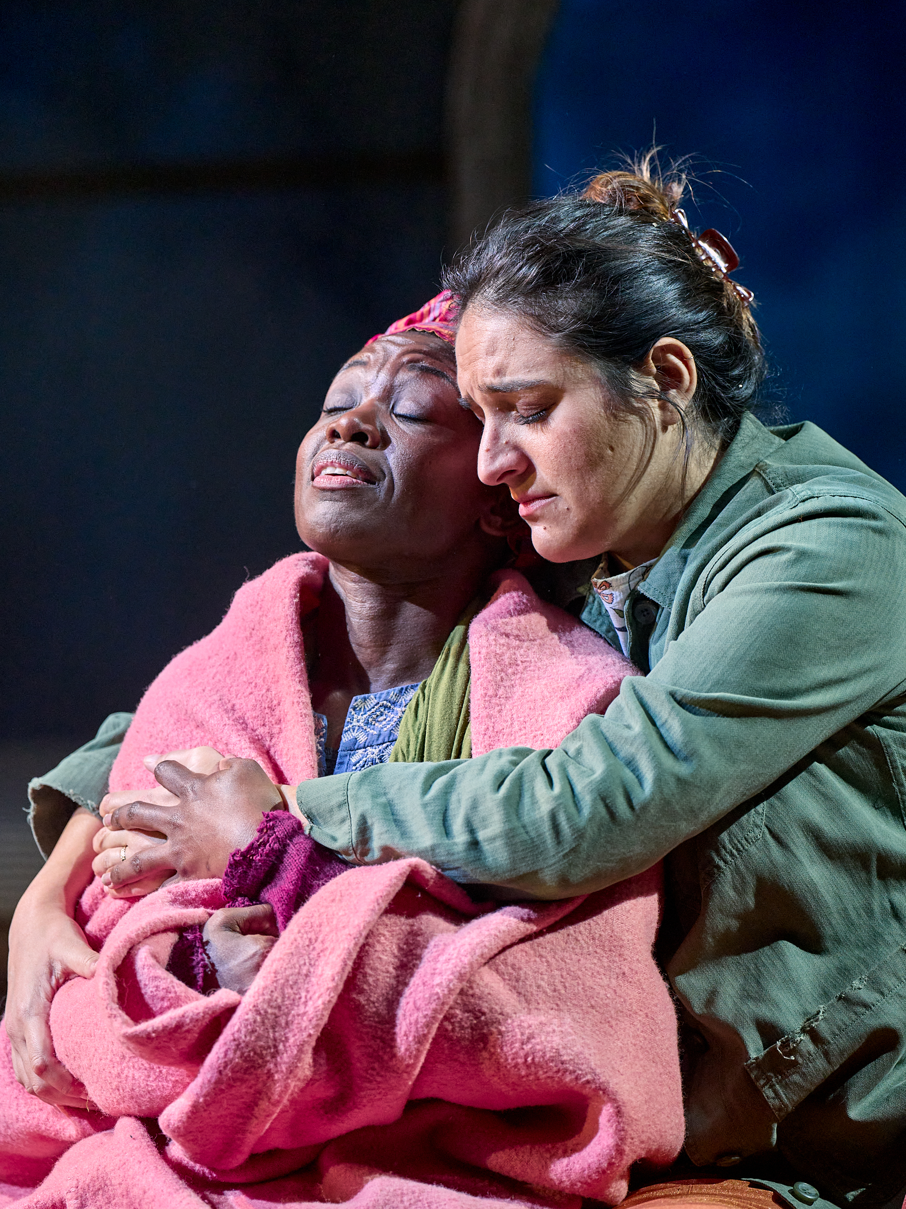 Two women sit looking exhausted, one holds the other