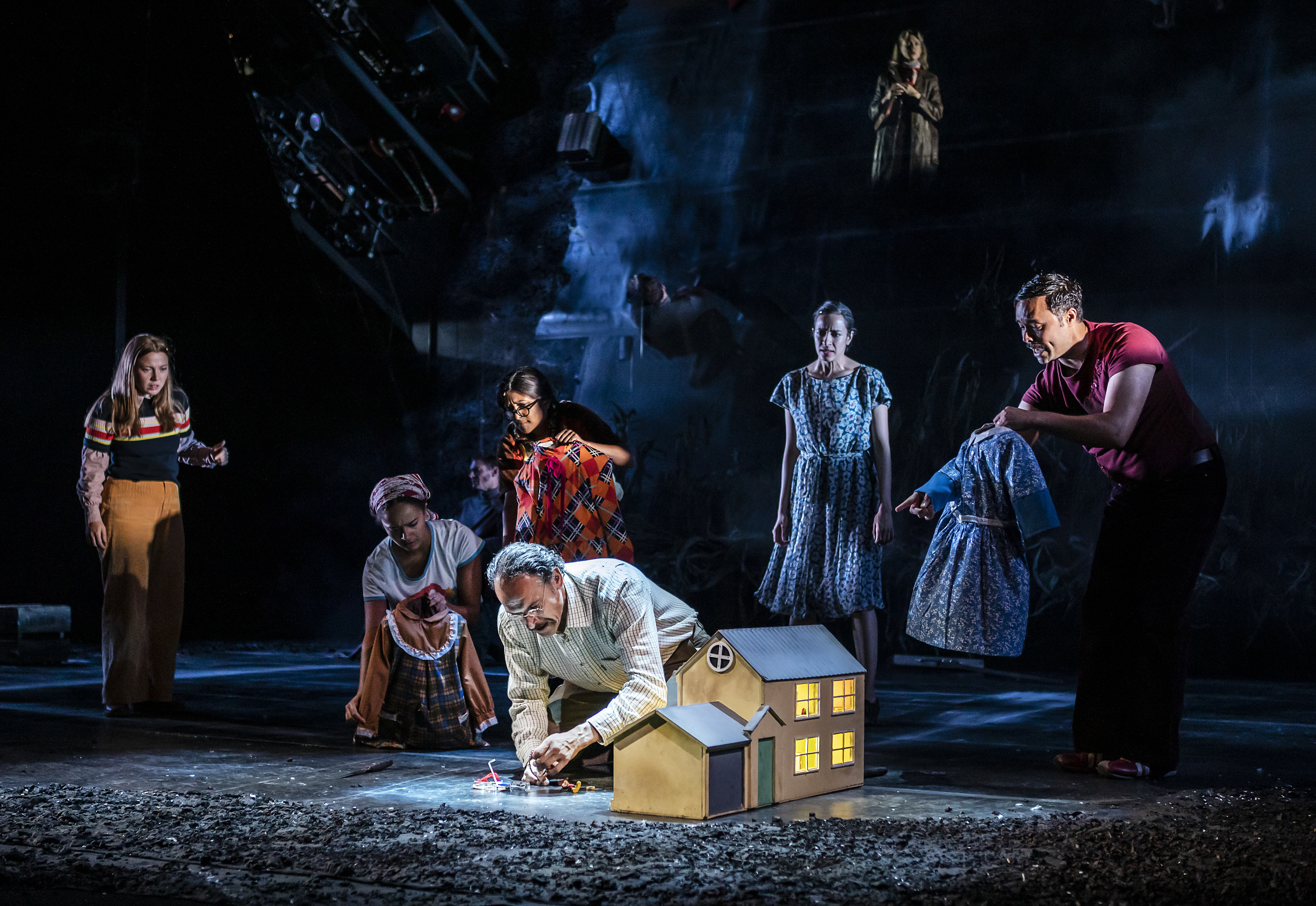 A group of people watch a man play with a dolls house