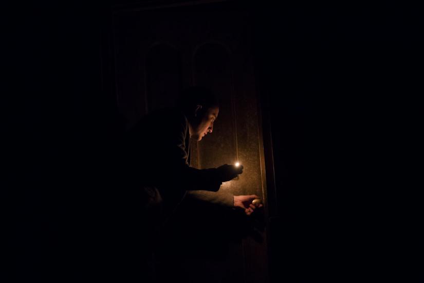 Man holds a small light as he goes to open a door.