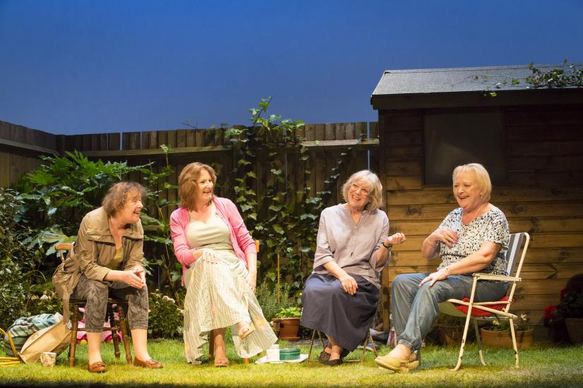 4 women sit in a garden, talking and laughing