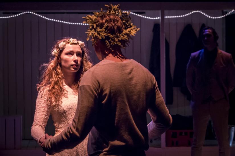 A woman, with flowers in her hair, gazes at a man as they hold hands.