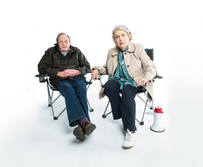 A man and woman sit in folding chairs looking at the camera.