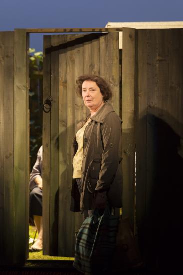 A woman stands in front of an open garden gate.