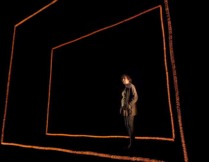 A woman stands, facing the audience, between two red rectangles