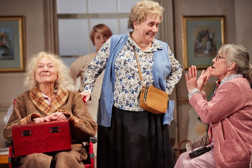 3 Elderly residents, one stands, one sits and one sits in a wheelchair