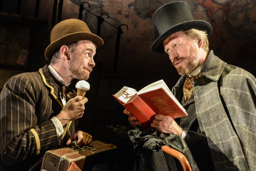 A man eats an ice cream as another reads a large red book