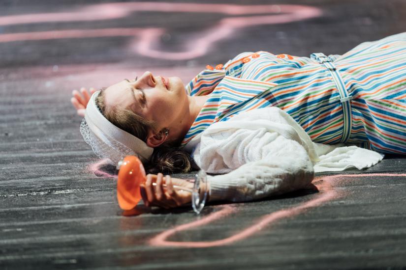 A woman lays on the floor holding a cocktail glass in the outline of a body