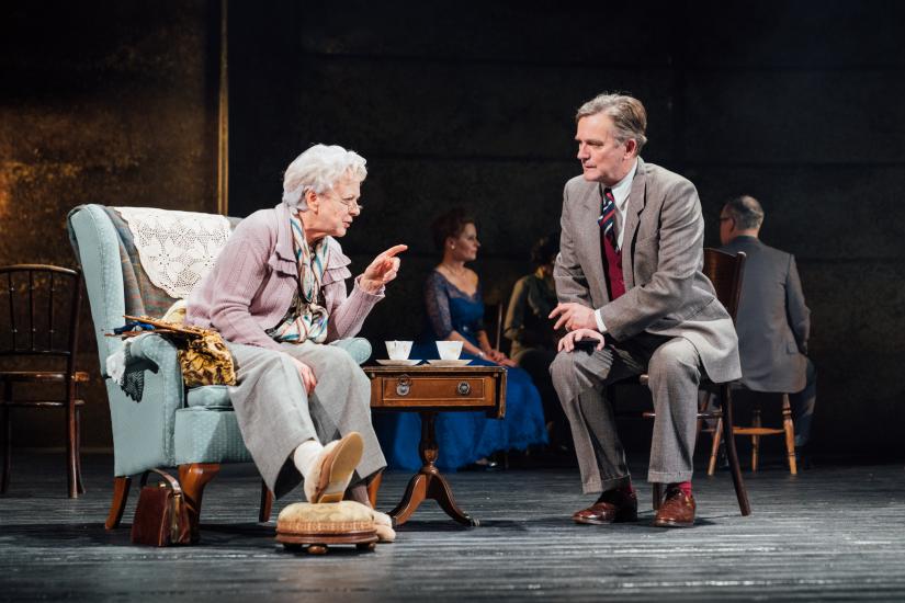 An older woman sits in a comfy chair talking to a man in a suit