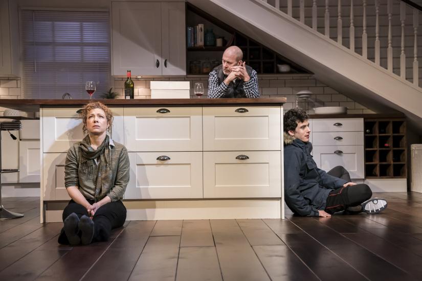 A man, woman and teenage boy sit around a kitchen staring intensely