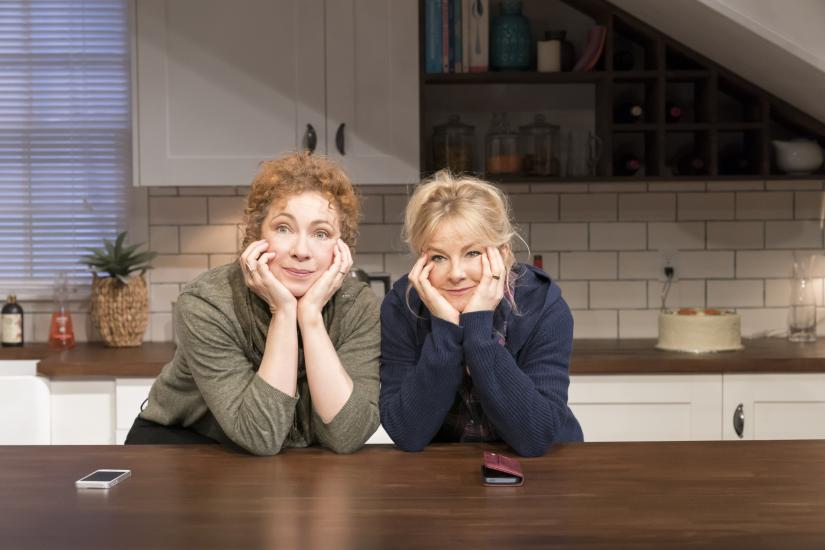 Two women lean on a kitchen counter smiling