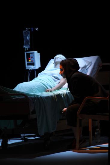 A man with bandages over his eyes lies in a hospital bed, a woman sits next to him worried