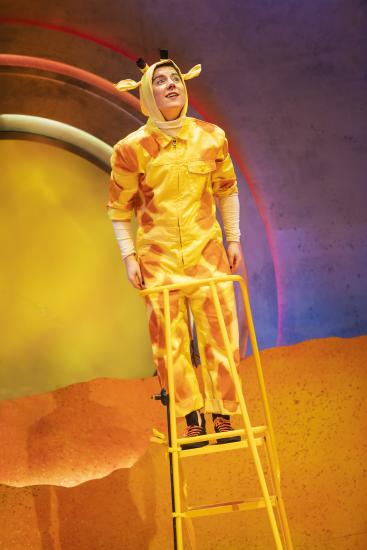 A man dressed as a yellow giraffe stands tall on a ladder
