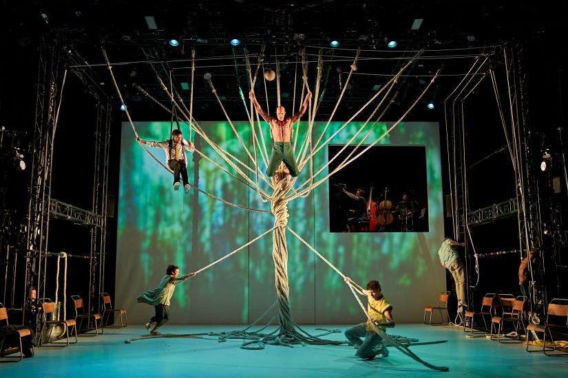 A man hangs in ropes as others wrap them around him