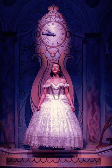 Cinderella wears a beautiful ball gown, and stands infront of a large clock