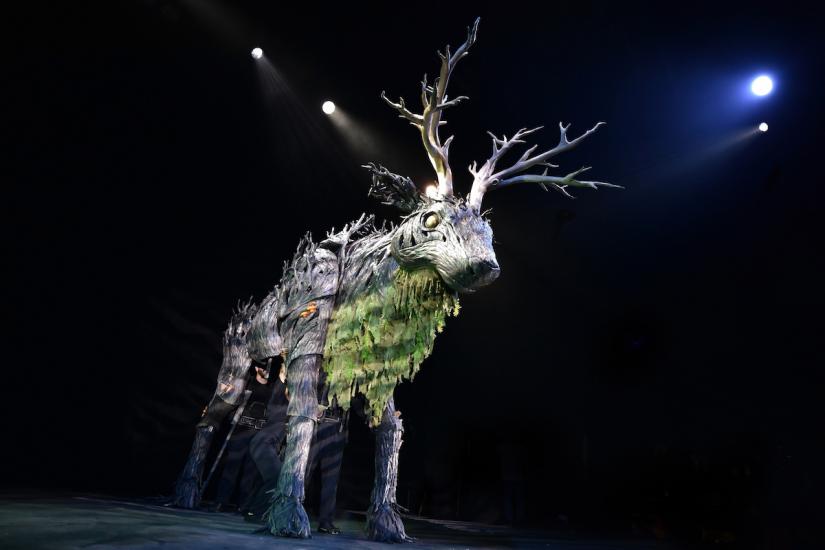A large moose-like creature, with great antlers, prowls the stage
