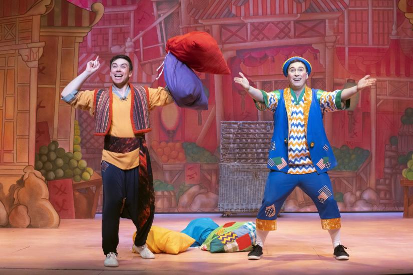 Aladdin and Wishy Washy wave their hands at the audience, they are holding bags of laundry