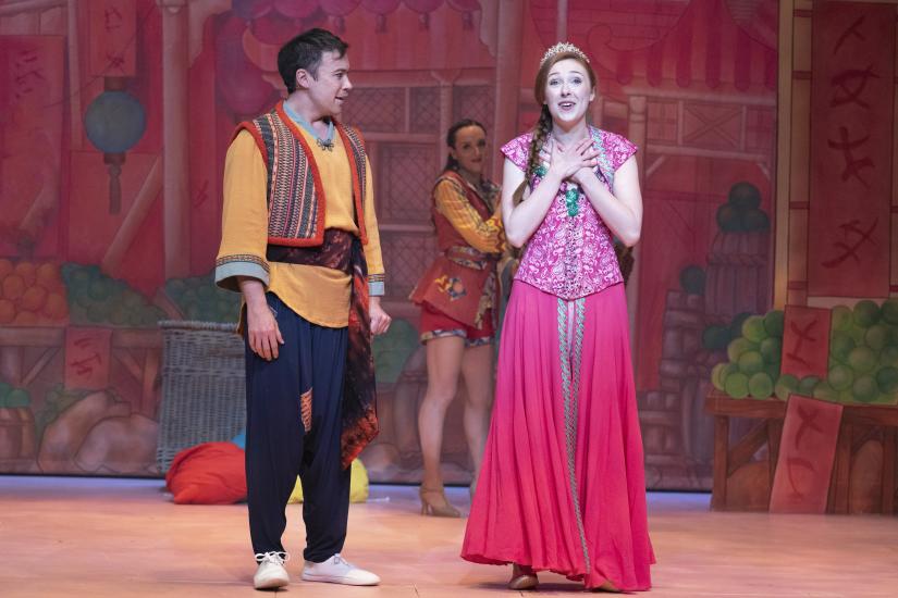 Aladdin and Princess Poppy stand together, Princess Poppy is looking longingly into the audience and smiling