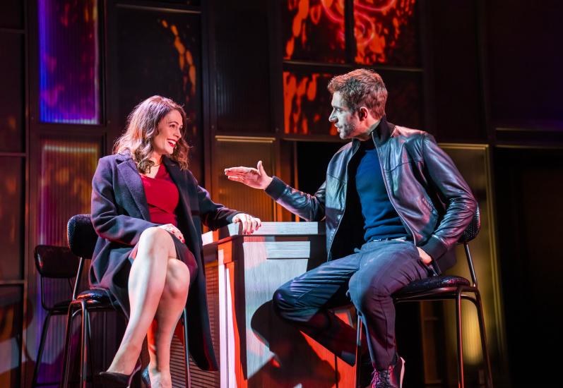 A man and a woman sit on bar stools chatting and laughing