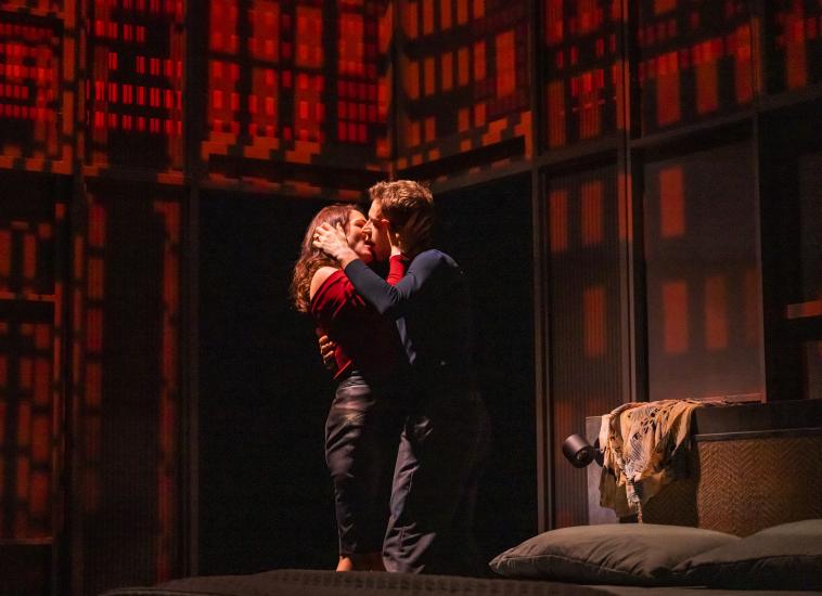 A man and a woman kiss passionately, the room is dark red behind them