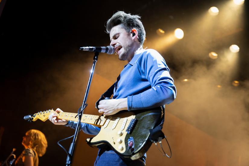 A man in a blue suit plays electric guitar