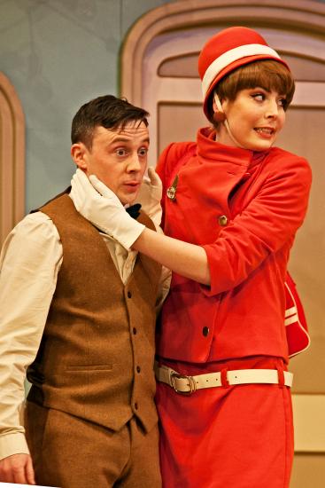 An air hostess wearing a red uniform stands next to a man in a suit, she is covering his ears