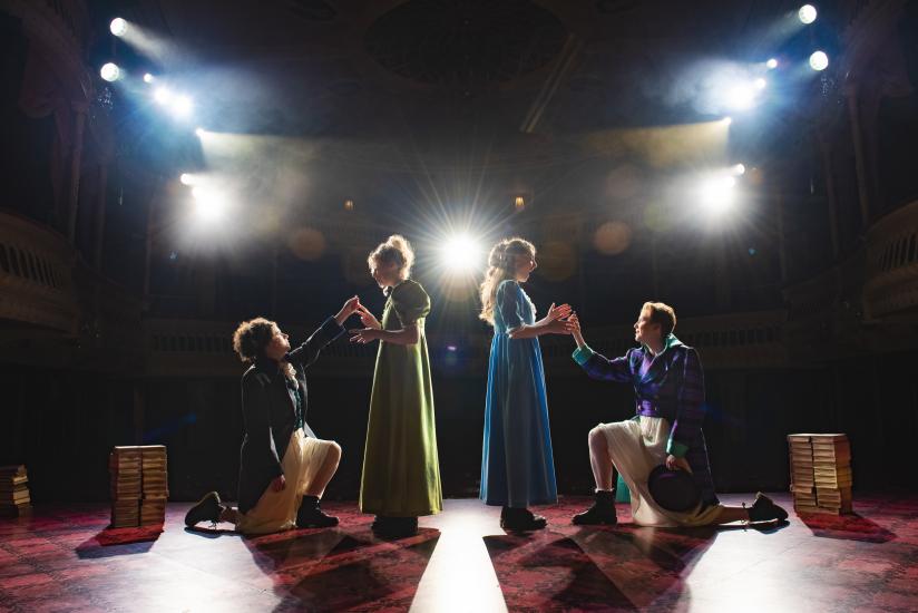 Two women stand in front of two men, the men are down on one knee proposing