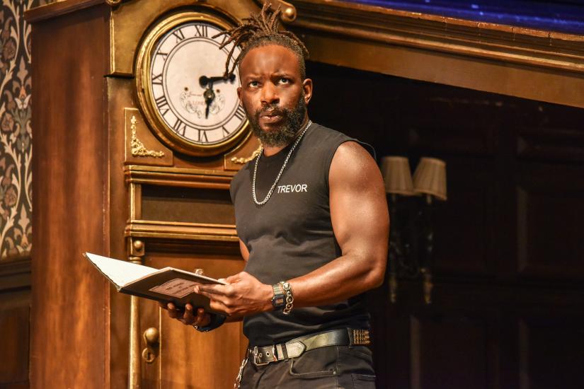 A man with the name 'Trevor' on his black t-shirt is holding a book and looking quizzical at the camera