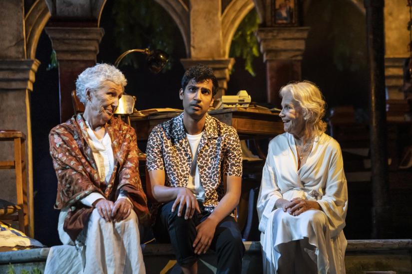 A young man sits between two women, who are looking at him and smiling