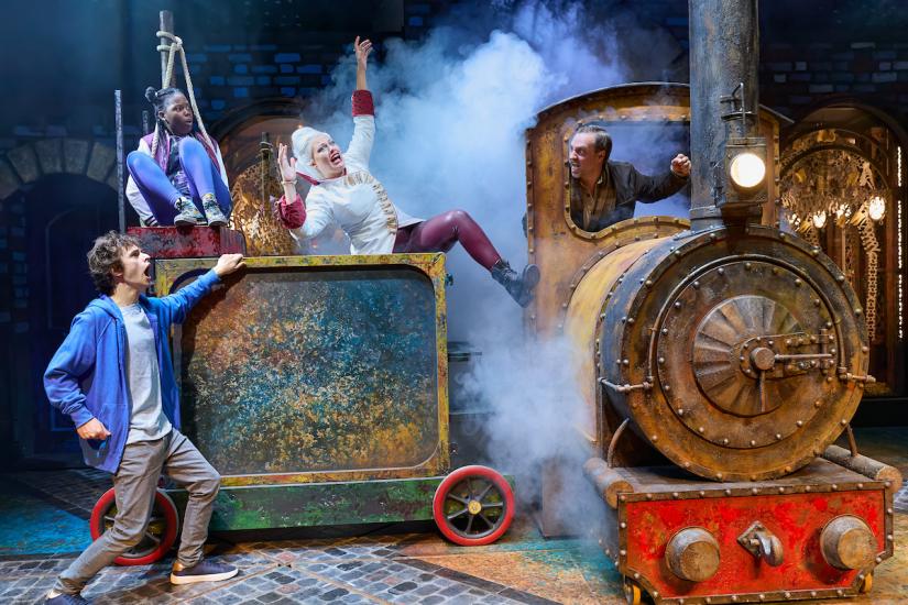 Smoke pours from a rusty train, its driver looking angrily at the white-haired woman, who appears to have been knocked by the train. The young boy and girl look on, shocked.