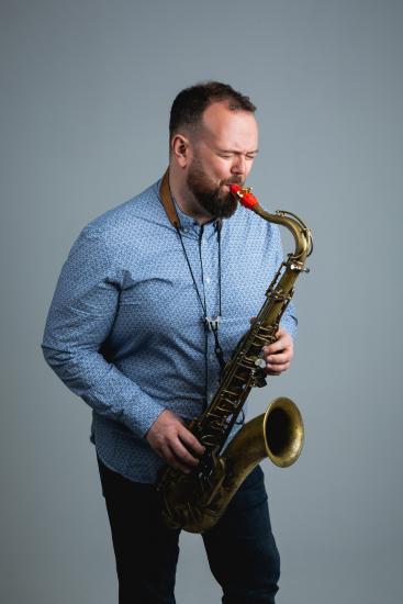 Dan Forshaw plays the saxophone in a star-patterned light blue shirt.