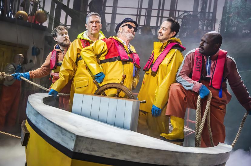 Five fishermen in a boat on the sea wearing yellow waterproofs and life jackets.