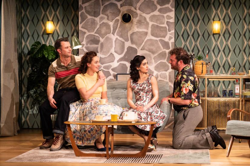 Two men and two women sit on a couch in front of a coffee table talking. 