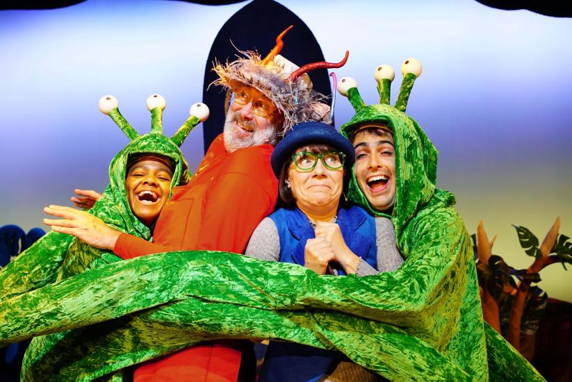 Two green aliens with three eyes and long arms wrap an orange and a blue alien in a big hug