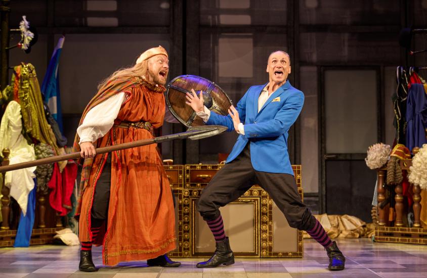 A viking man with a shield attacks another man wearing a blue jacket