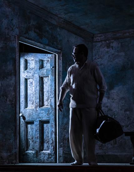 A silhouette of a man wearing cricket whites and holding a bag against a partially open door frame