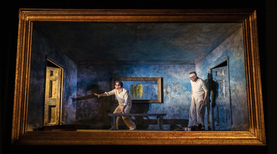 Two men stand in a blue room inside a ornate gold frame, they are reaching towards an open door
