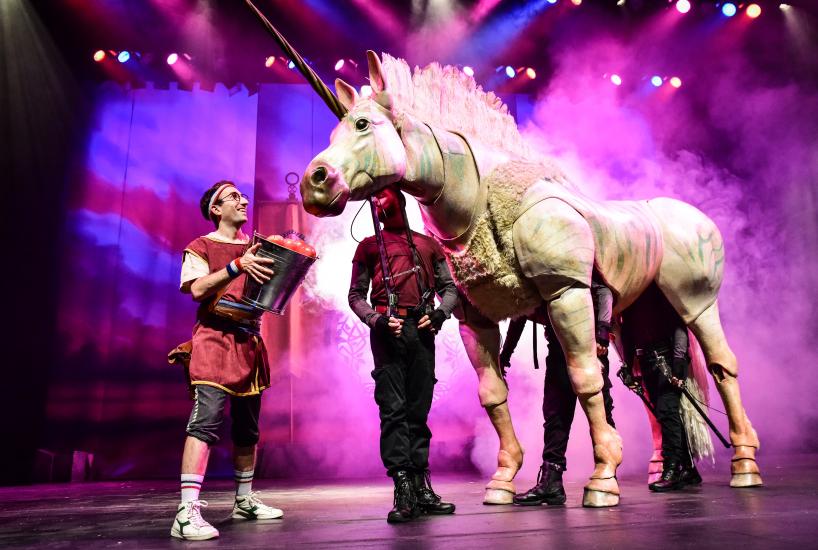 A man stands holding a bucket of red balls, looking up at a white unicorn