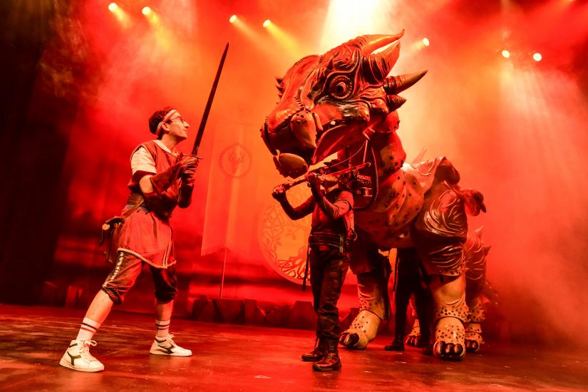 A man stands holding a sword up at a large dragon-like beast, the background is firey orange