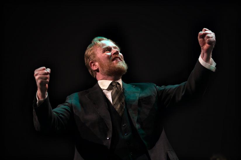 A man in a black suit looks to the sky, his hands are held in tight fists