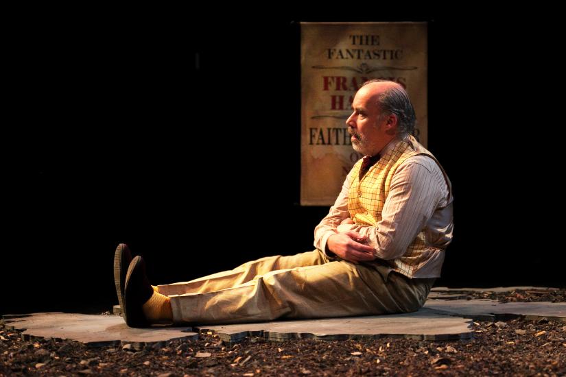 A older man is sitting on the floor, legs outstetched in front of him