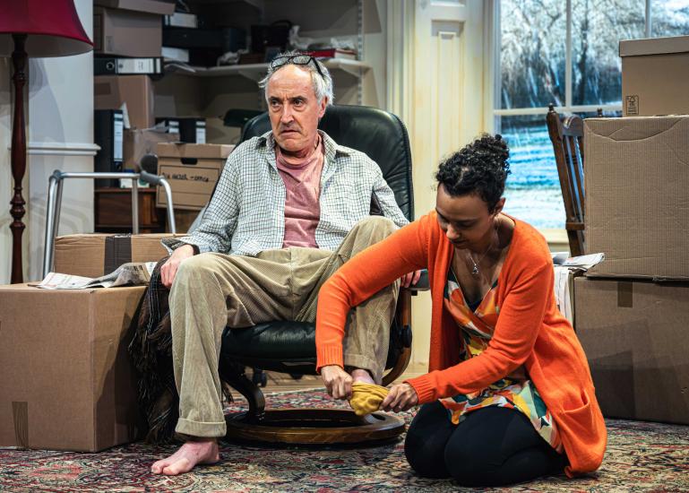 A woman sits on the floor beside an ageing man who looks dishevelled