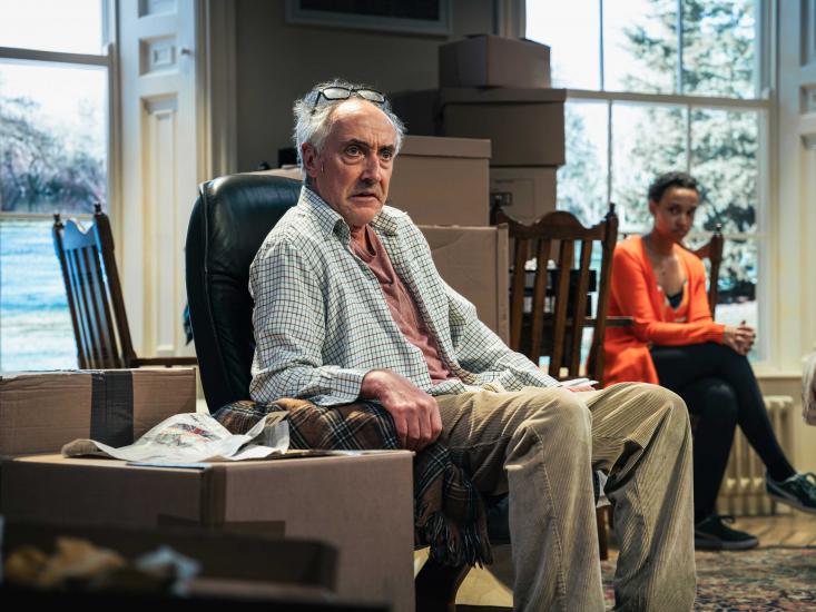An ageing man sits in a chair, he looks concerned