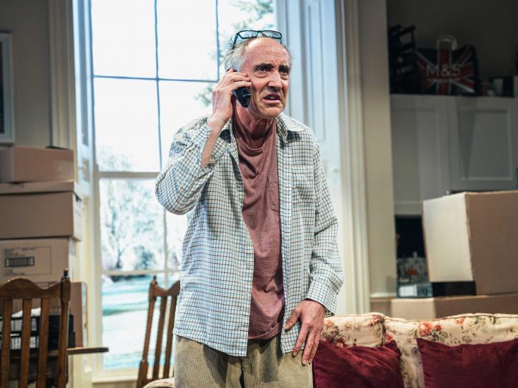 An ageing man holds a telephone to his ear, looks annoyed