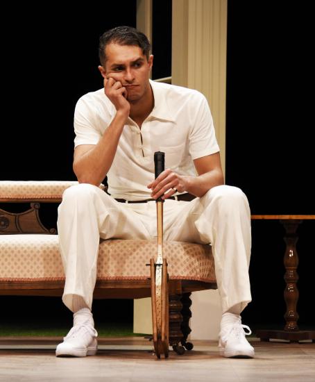 A man sits with his hand on face leaning on a racquet he's holding.