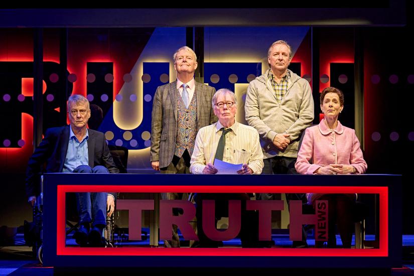 The cast of the news team stand and sit behind the TRUTH news desk