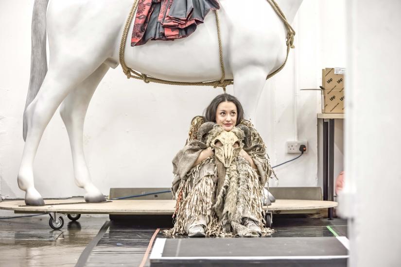 Woman sits under horse with a skull in hand